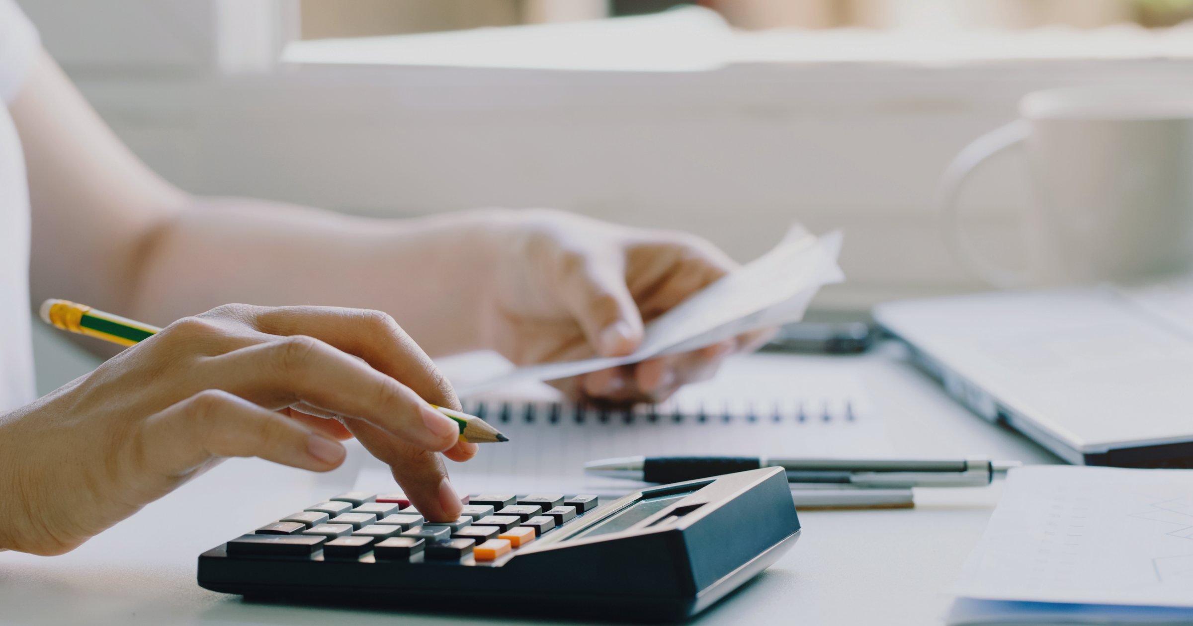 Persoană care calculează facturile casnice cu un calculator de birou, ținând o factură în mână, la masa de acasă